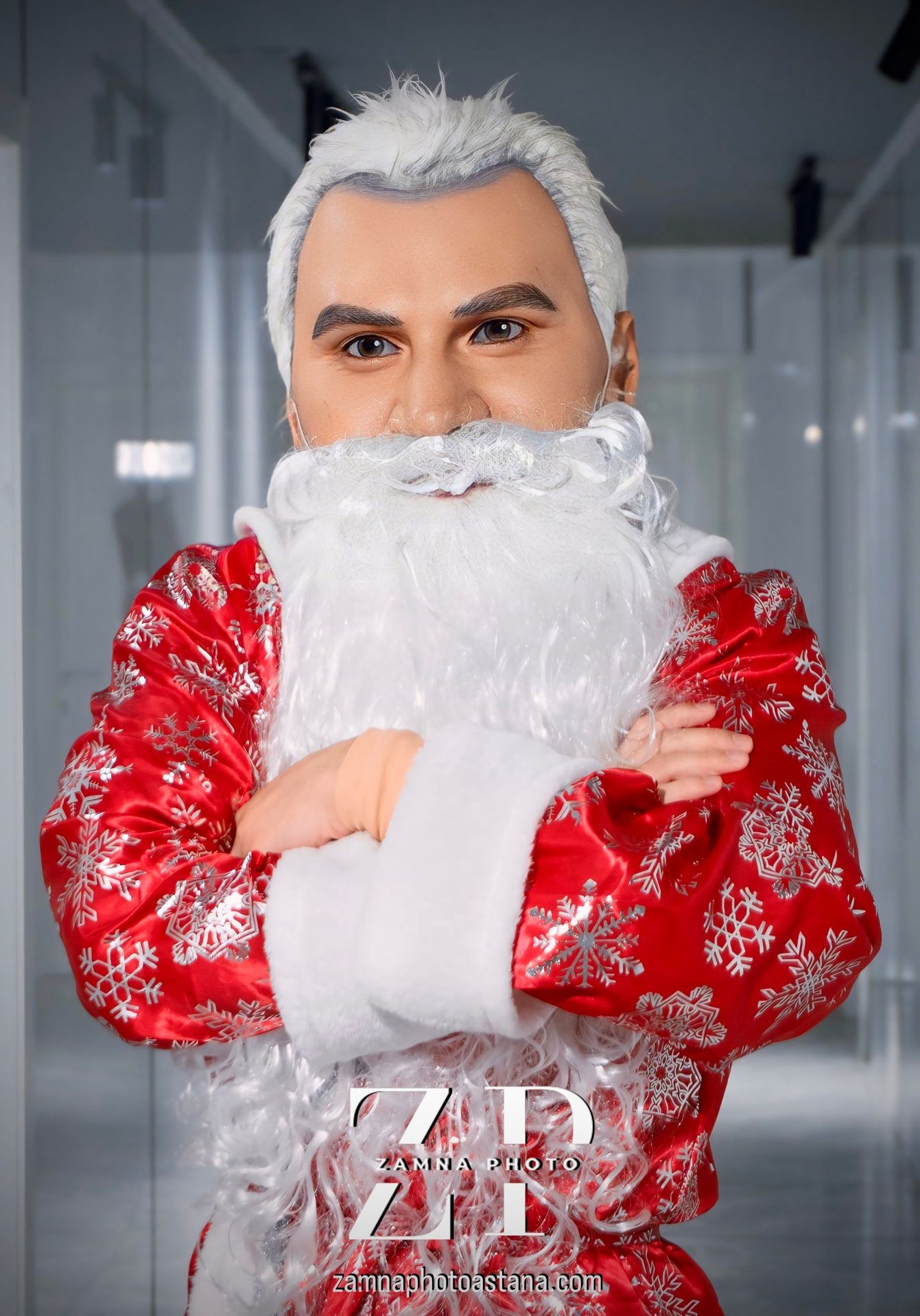 Person in a red snowflake-patterned costume with a white beard and wig, arms crossed.