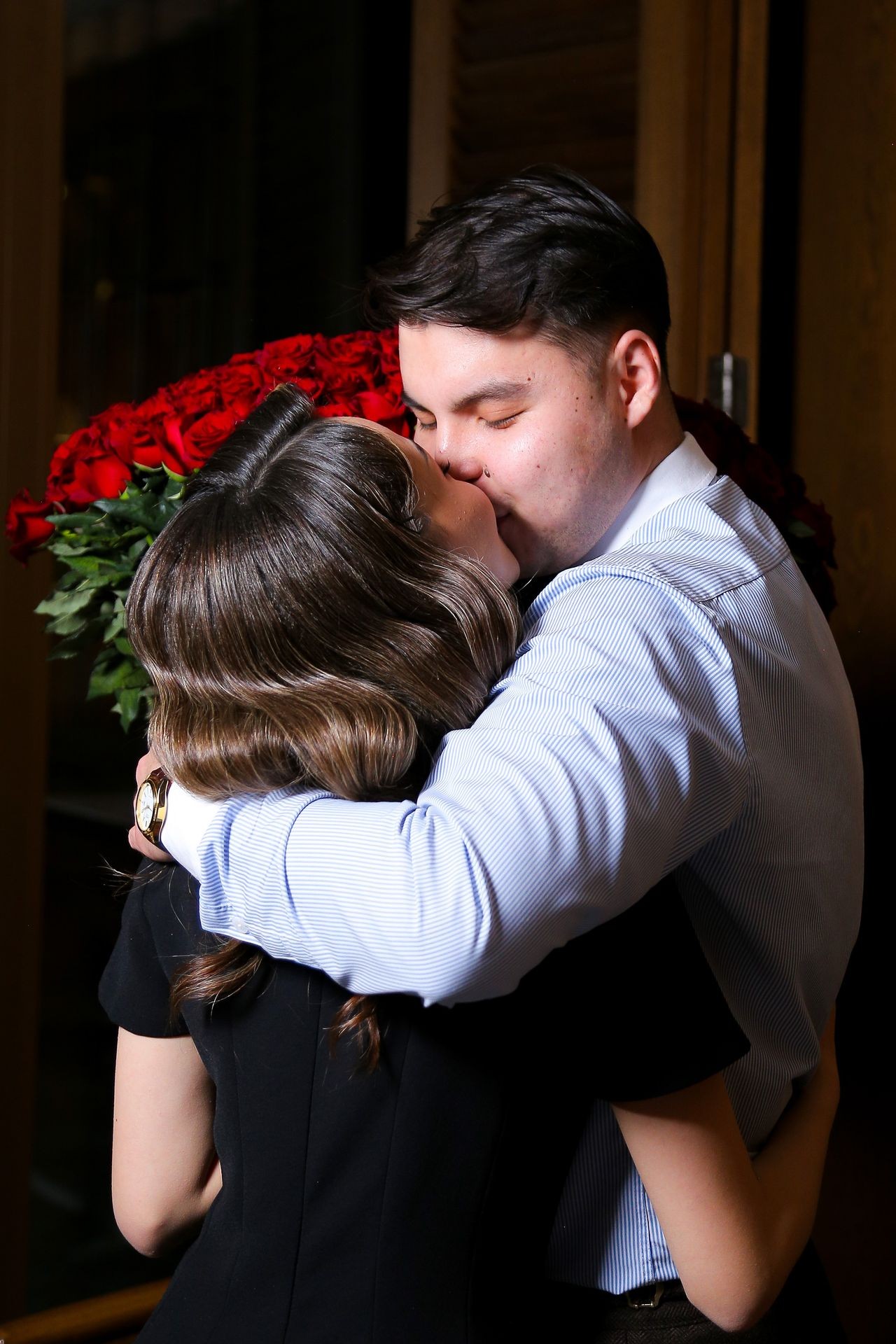 Couple embracing and kissing, holding a large bouquet of red roses.